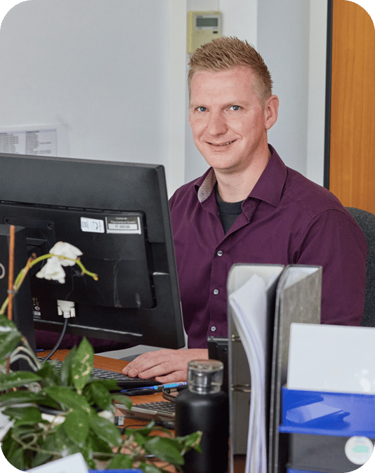 Chef d'équipe Service Client Homme sympathique avec une chemise couleur aubergine assis devant l'ordinateur et travaillant