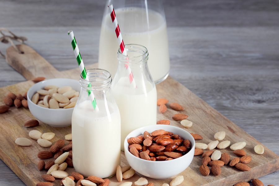 Recette de cocktail d'amandes sans alcool Image d'ambiance « cocktail d'amandes sans alcool » : deux bouteilles à col large remplies de pailles colorées se dressent sur une planche en bois avec des amandes