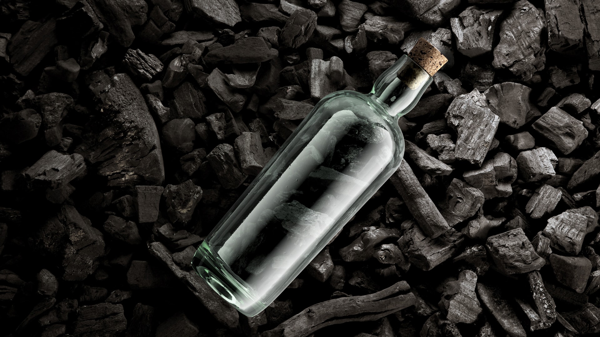 Fermetures d'Estal Corkcoal Image d'ambiance : une bouteille en verre transparent de la marque Estal avec un bouchon Corkcoal repose sur un fond de morceaux de charbon